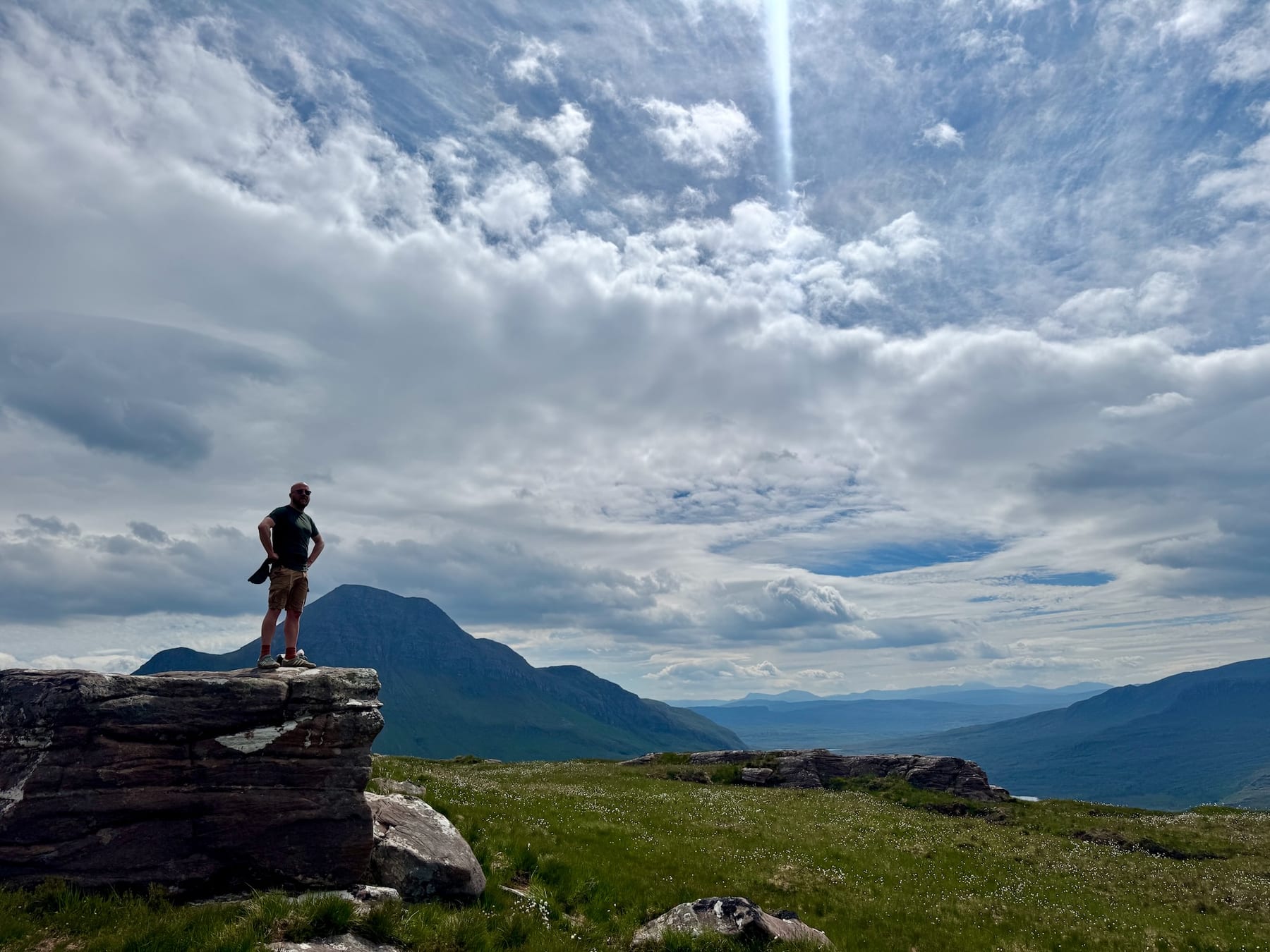 Heath standing on a rocky ledge beneath a vast Highland sky